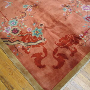 Coral high-pile rug with colorful floral motifs, an olive border, resting on worn wood planks.
