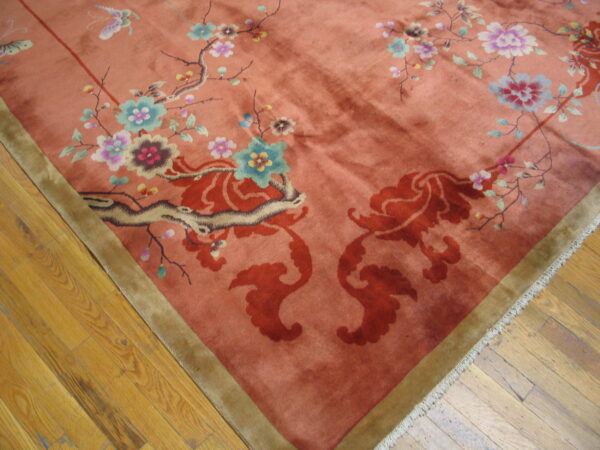 Coral high-pile rug with colorful floral motifs, an olive border, resting on worn wood planks.