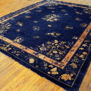 Plush, deep blue rug with scattered gold botanical patterns and a broad tan border shown on hardwood flooring.