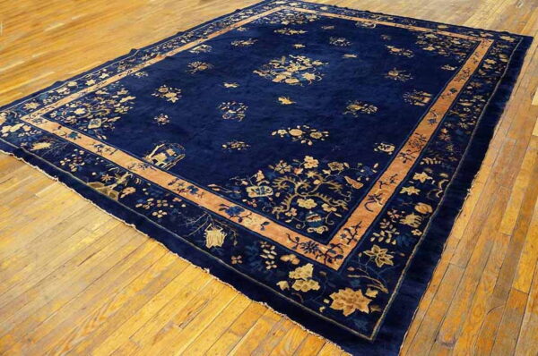 Plush, deep blue rug with scattered gold botanical patterns and a broad tan border shown on hardwood flooring.