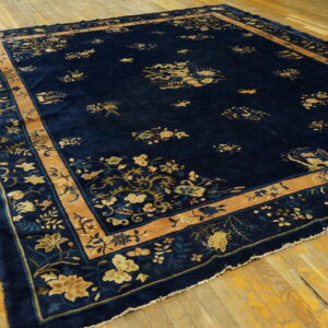 Dark blue high-pile rug with tan and gold intricate floral designs displayed on distressed yellow wood flooring.