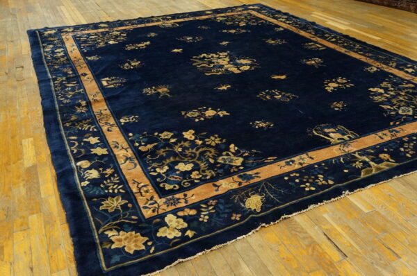 Dark blue high-pile rug with tan and gold intricate floral designs displayed on distressed yellow wood flooring.