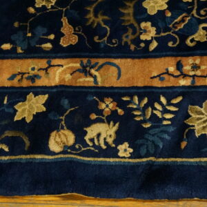 Detailed navy blue rug with golden floral patterns and a wide rust-colored border on wood floor.