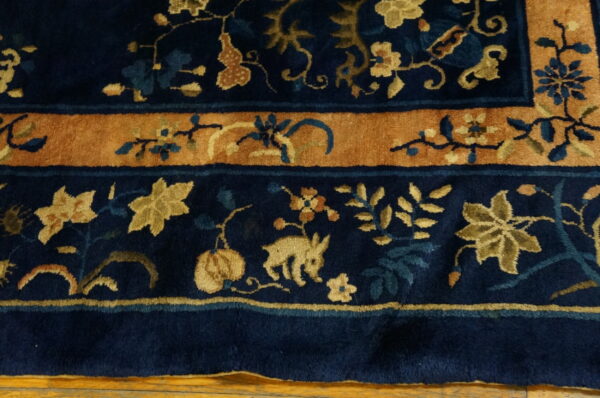 Detailed navy blue rug with golden floral patterns and a wide rust-colored border on wood floor.