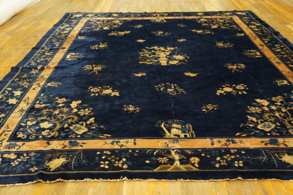Deep blue high-pile rug featuring scattered gold and teal floral designs and a wide camel border on a wood floor.