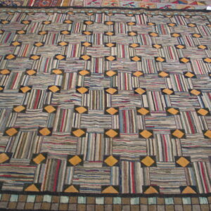 Geometric rug featuring alternating striped rectangles and orange diamonds, framed by a tiled border.