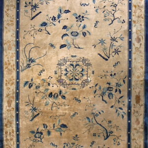 A tan rug with scattered indigo blue floral sprays and a detailed vase and vine border.