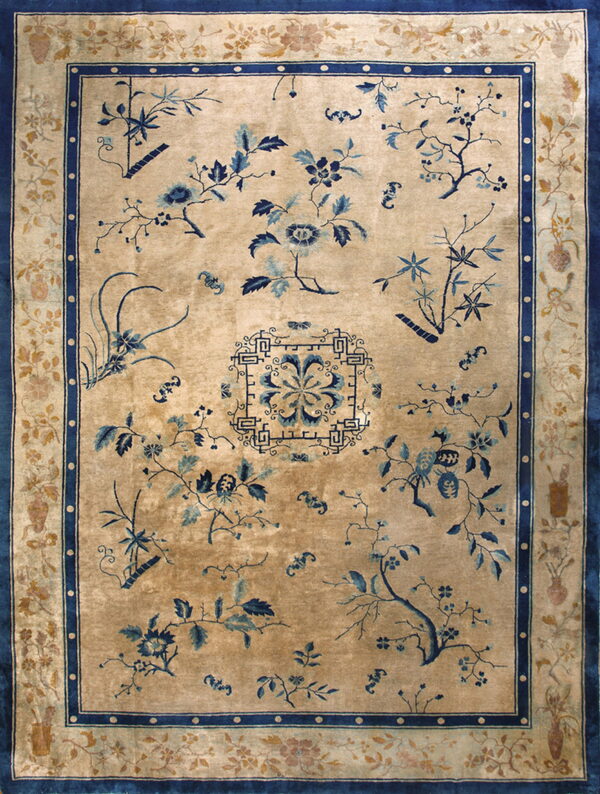 A tan rug with scattered indigo blue floral sprays and a detailed vase and vine border.
