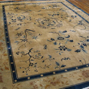 Gold rug with high sheen, dark blue floral patterns, and multi-layered borders resting on wood plank flooring.