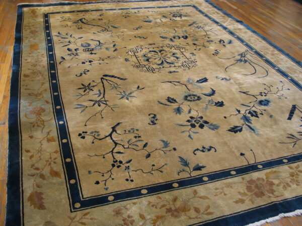 Gold rug with high sheen, dark blue floral patterns, and multi-layered borders resting on wood plank flooring.