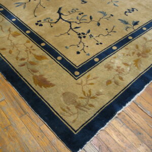 Gold and blue floral rug corner with wide borders resting on worn plank hardwood flooring.