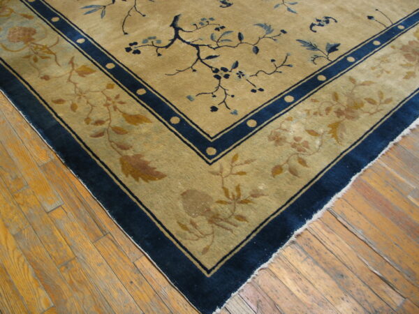 Gold and blue floral rug corner with wide borders resting on worn plank hardwood flooring.