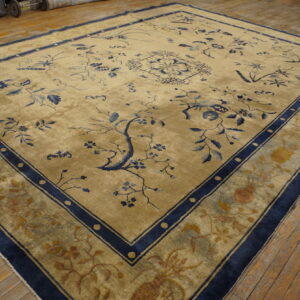 Tan large area rug with intricate blue floral motifs and wide navy borders on distressed hardwood.