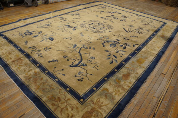 Tan large area rug with intricate blue floral motifs and wide navy borders on distressed hardwood.