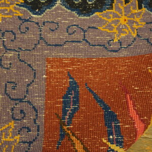 Flatweave rug detail with purple border, rust field, and blue geometric patterns rests on wooden planks.
