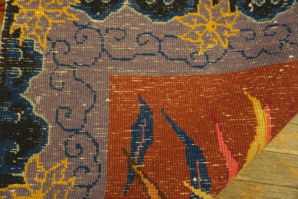 Flatweave rug detail with purple border, rust field, and blue geometric patterns rests on wooden planks.