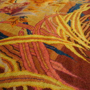 Close-up of a dense pile rug showing yellow and pink foliage against a deep rust background.