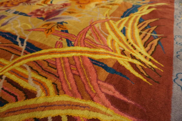 Close-up of a dense pile rug showing yellow and pink foliage against a deep rust background.