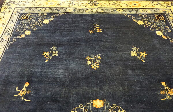 Deep indigo rug field with scattered gold florals and an ornate, wide cream and blue border.