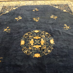A deep navy blue rug features a gold floral medallion and a complex cream-colored border on hardwood flooring.