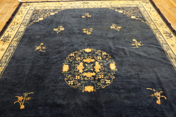 A deep navy blue rug features a gold floral medallion and a complex cream-colored border on hardwood flooring.