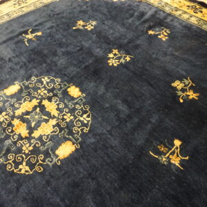 Deep blue plush rug with gold floral designs and complex border resting on light wooden planks.