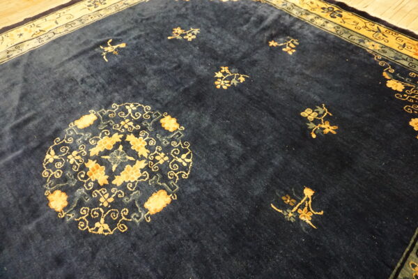 Deep blue plush rug with gold floral designs and complex border resting on light wooden planks.