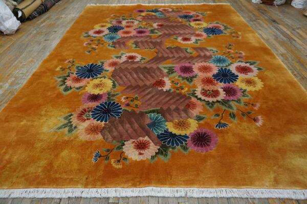 Velvety saffron rug with carved multicolored floral and brown geometric patterns rests on distressed wood flooring.