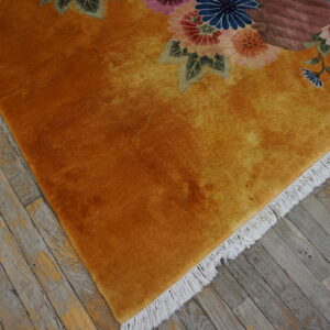 A plush golden-orange rug with carved floral patterns sits on rustic gray wood flooring.