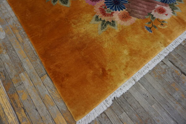 A plush golden-orange rug with carved floral patterns sits on rustic gray wood flooring.