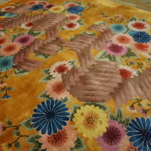 Gold rug with vibrant multicolor florals surrounding a sculpted brown geometric design.