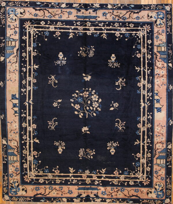 Navy blue rug with pale pink and beige borders, featuring intricate floral and architectural designs on a wood floor.