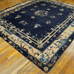 Dark blue rug with tan and light blue floral and pagoda motifs on a plank wood floor.