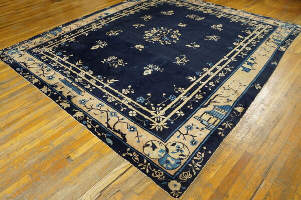 Dark blue rug with tan and light blue floral and pagoda motifs on a plank wood floor.