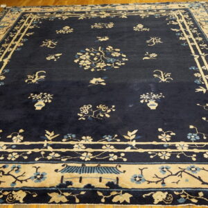 Dark blue rug with contrasting cream and light blue botanical and architectural patterns on hardwood flooring.