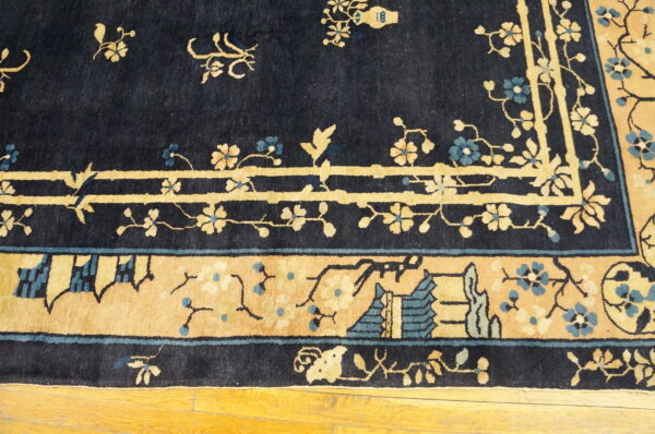 Detail of a dark blue rug featuring tan and teal floral patterns and architectural border on wood flooring.