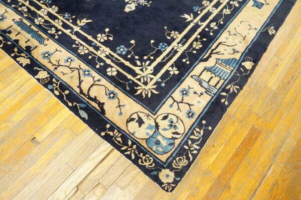 Dark blue and beige rug corner with intricate floral and pavilion patterns resting on wood planks.