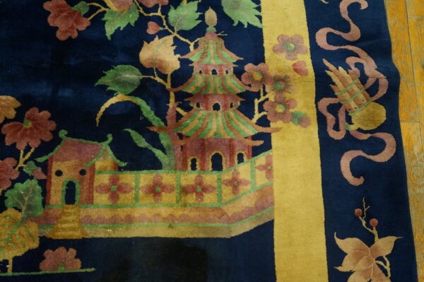 Dark blue rug patterned with a colorful pagoda, foliage, and a broad mustard yellow border stripe on wood flooring.