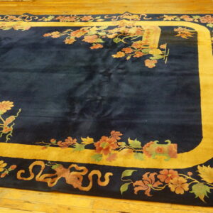 Navy blue rug with a gold border framed by muted floral and vine patterns on wood flooring.