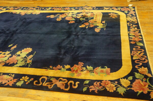 Navy blue rug with a gold border framed by muted floral and vine patterns on wood flooring.