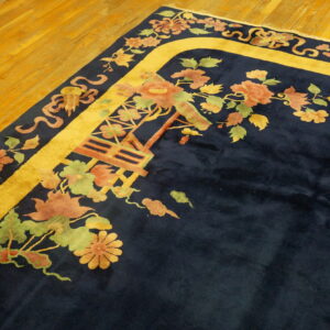 Navy high-pile rug featuring a gold border and colorful floral motifs rests on wooden plank flooring.