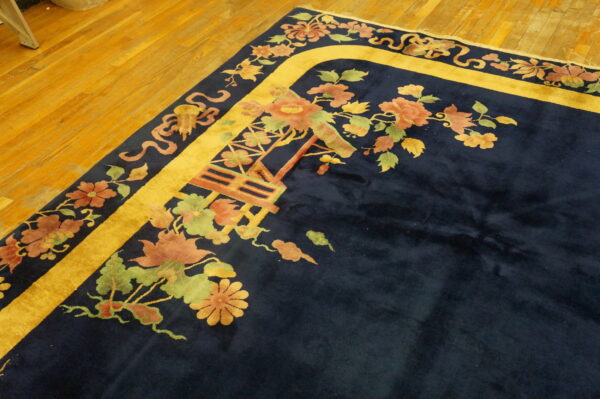 Navy high-pile rug featuring a gold border and colorful floral motifs rests on wooden plank flooring.