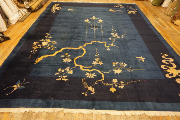 Large deep blue rug featuring a bold gold floral and bird pattern on wood planks.