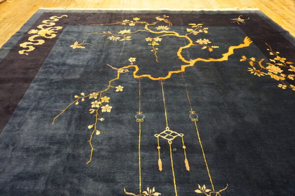 Deep blue rug with gold cherry blossom branches, birds, and decorative knot patterns on a wood floor.