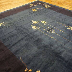 Deep blue rug with gold floral and avian patterns and a dark border rests on light wood flooring.
