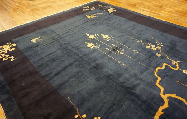 Deep blue rug with gold floral and avian patterns and a dark border rests on light wood flooring.