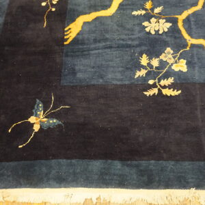 Navy and teal high-pile rug detail showing gold botanical pattern, a butterfly, and white fringe on wood floor.
