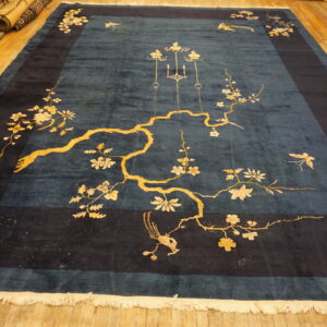 Large teal blue rug with a dark border, featuring a yellow flowering branch, birds, and butterflies on a wood floor.