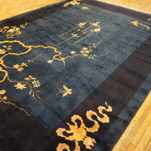 A dark blue rug with gold flowering branches and birds rests on a distressed yellow hardwood floor.