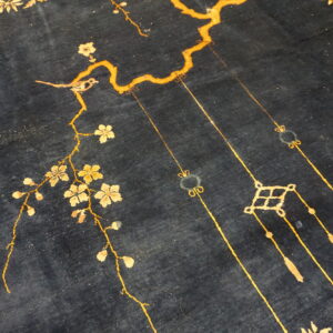 Deep blue rug surface displays a gold and beige pattern of flowering branches, a small bird, and hanging tassels.